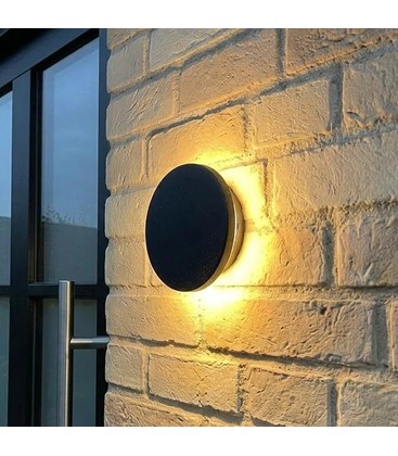 Moderne sort utendørs vegglampe montert på en mørk husvegg som gir stemningsfull belysning.